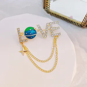Vista macro de broche dorado LOVE con planeta de strass y cadenas de estrellas colgantes
