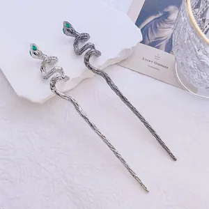 Detailed view of two vintage silver snake hair pins with green rhinestone eyes on stone