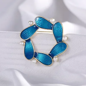 Elegant gold-tone brooch with blue enamel petals and white pearls on white silk