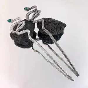 Detail of silver snake hair pin with green gemstone on volcanic rock with reflection