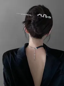 Detail of silver snake-shaped hair pin and necklace with green gemstones on model