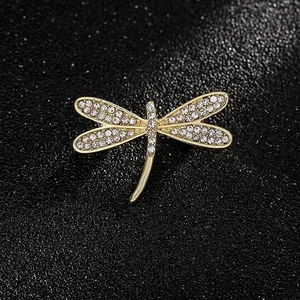 Elegante spilla a forma di libellula dorata con cristalli bianchi su sfondo di pelle nera
