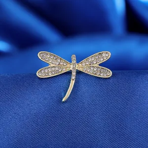 Elegante spilla a libellula dorata con cristalli su sfondo in seta blu scuro