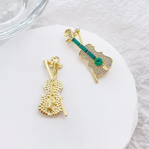 Broche violon verte sertie de strass et perle blanche sur une base dorée élégante