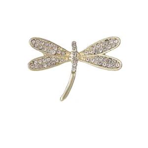 Squisita spilla a libellula dorata con strass bianchi scintillanti su sfondo bianco