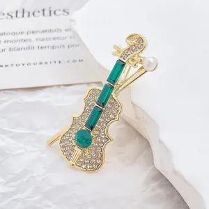 Détails de la broche violon avec pierres émeraude, strass blancs et perle élégante
