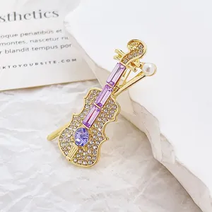 Broche violon ornée de strass violets et d'une perle blanche sur monture dorée