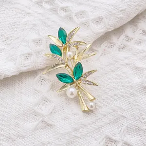Broche en bambou doré avec cristaux vert émeraude et perles blanches sur tissu tricoté