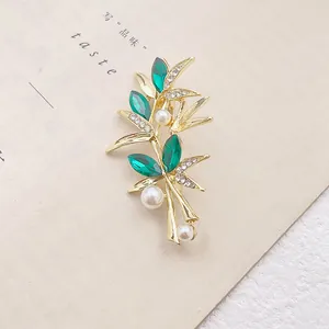 Broche élégante feuille de bambou dorée avec cristaux émeraude et perles sur fond neutre