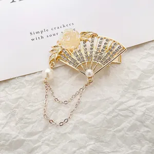 Chinese style fan hair clip with gold metal fringe and pearls on white textured background