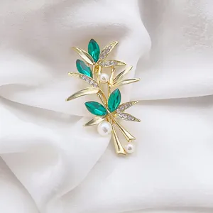 Gros plan d'une broche bambou avec cristaux verts et perles sur soie blanche
