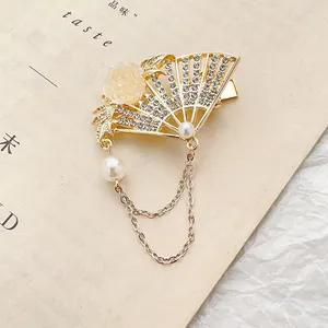 Golden folding fan hair clip with white rhinestones and pearls on vintage book page