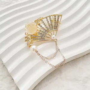 Detail of a golden fan-shaped hair clip with white rhinestones and pearl tassels