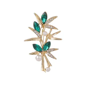 Broche bambou élégante en or avec cristaux verts et perles sur fond blanc pur