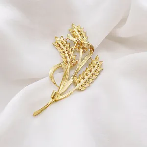 Exquisite golden wheat ear brooch with polished metallic texture on a white silk background