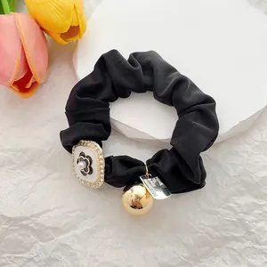 Detail of camellia floral charm and engraved gold pendant on black silk scrunchie