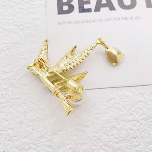 Golden bird brooch with white pearl and green teardrop gemstone on white background