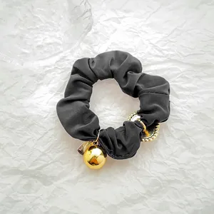 Detail of black fabric scrunchie featuring elegant gold metal charms and premium texture