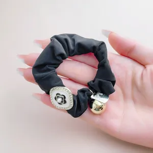 French camellia scrunchie with pearls and rhinestones held in hand against beige background