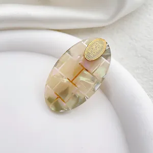 Detalle macro de pinza de pelo ovalada en acetato con patrón de cuadros iridiscentes y oro