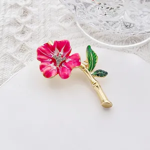 Macro detail of enamel flower brooch with pink petals, green leaves and crystal center