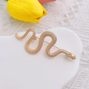 Dettaglio spilla a forma di serpente dorata con trama a squame su piatto bianco