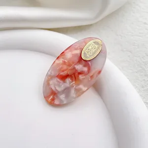 Detalle de pinza para el pelo de acetato jaspeado rosa y blanco con logo dorado oval