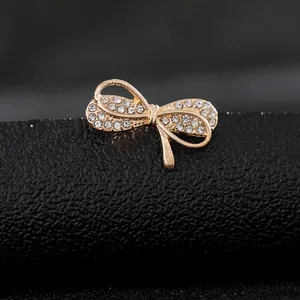 Vista macro de broche de lazo dorado con circonitas blancas sobre cuero negro texturizado