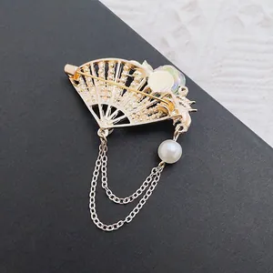 Detailed macro view of golden folding fan brooch with white pearl tassels and chain