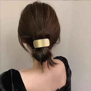 Detailopname van een matgouden rechthoekige haarclip gestyled op een chique haarknot