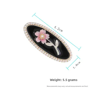 Detail of a vintage oval hair clip featuring a pink flower, pearls, and gold leaves