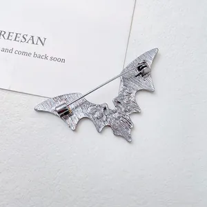 Silver bat wing brooch with back pin fastener on a minimalist textured white background