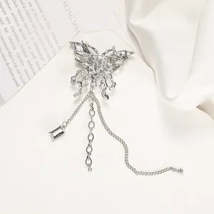 Silver butterfly brooch with long metal tassels and crystal pendant on white silk background