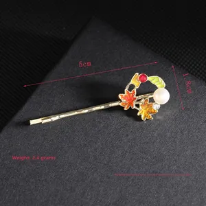 Detail view of a 5cm golden maple leaf hair clip with pearls and red rhinestones