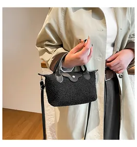 Detail of black fuzzy dumpling bag with leather handle worn by model in a beige coat