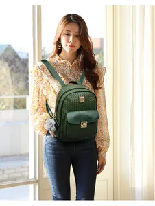 Close-up of a green PU leather backpack with gold buckle and grey pompom keychain