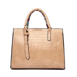 Close-up of khaki crocodile pattern handbag with elegant floral silk scarf on handle