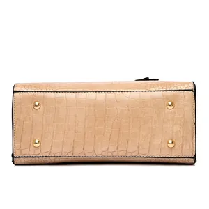 Detailed base view of beige handbag showing croc-embossed texture and four gold protective feet