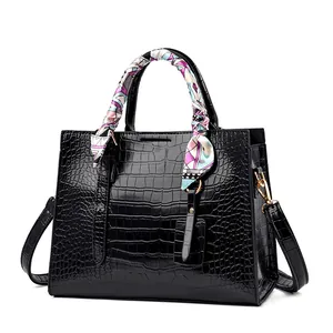 Close-up of black crocodile pattern tote bag featuring decorative silk scarf handles