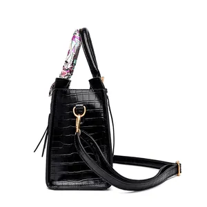 Close-up of black crocodile pattern tote bag with decorative silk scarf and gold hardware