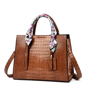 Detailed macro view of brown crocodile-embossed leather tote bag with silk scarf handle