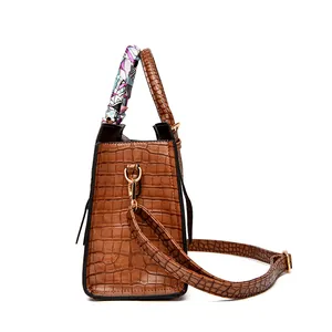 Detail of brown crocodile embossed tote bag with decorative silk scarf and gold metal hardware