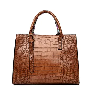 Close-up of brown crocodile embossed leather handbag with decorative printed silk scarf handle