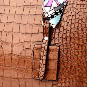 Detail of brown crocodile pattern handbag featuring gold hardware and a colorful silk scarf