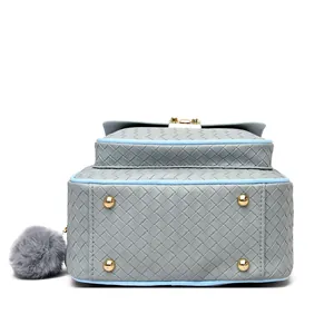 Close-up of woven gray leather backpack base with gold metal feet and blue piping detail