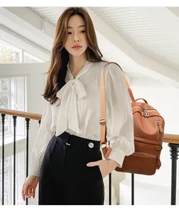 Modieuze bruine PU-leren rugzak getoond met elegante strikblouse en zwarte broek