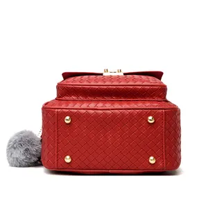 Detail of red woven leather backpack with gold protective studs and plush pompom charm