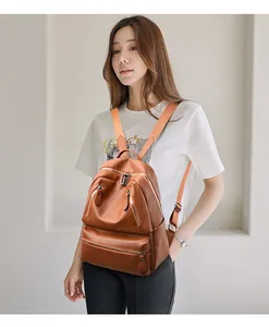 Brown PU leather backpack detail with front zippers and orange woven straps on a model