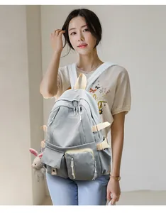 Detailed side view of a gray nylon backpack with cream straps and cute plush pendant