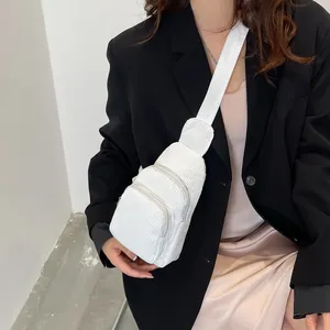 Detailed close-up of white corduroy crossbody bag texture on model with black blazer